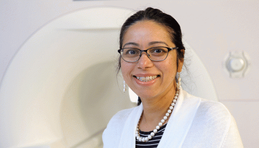 Dr. Fatima Husain standing next to magnetic resonance imaging machine